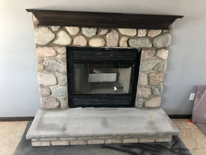 Indoor fieldstone fireplace with a timber mantel and poured concrete hearth