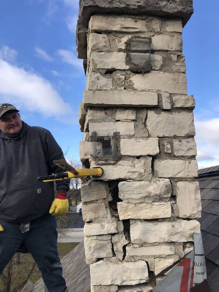 Tim Kempen on a roof next to a limestone chimney with wide structural cracks and separating joints